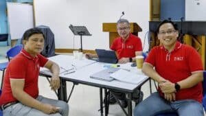 Three men in red shirts sitting at a table.